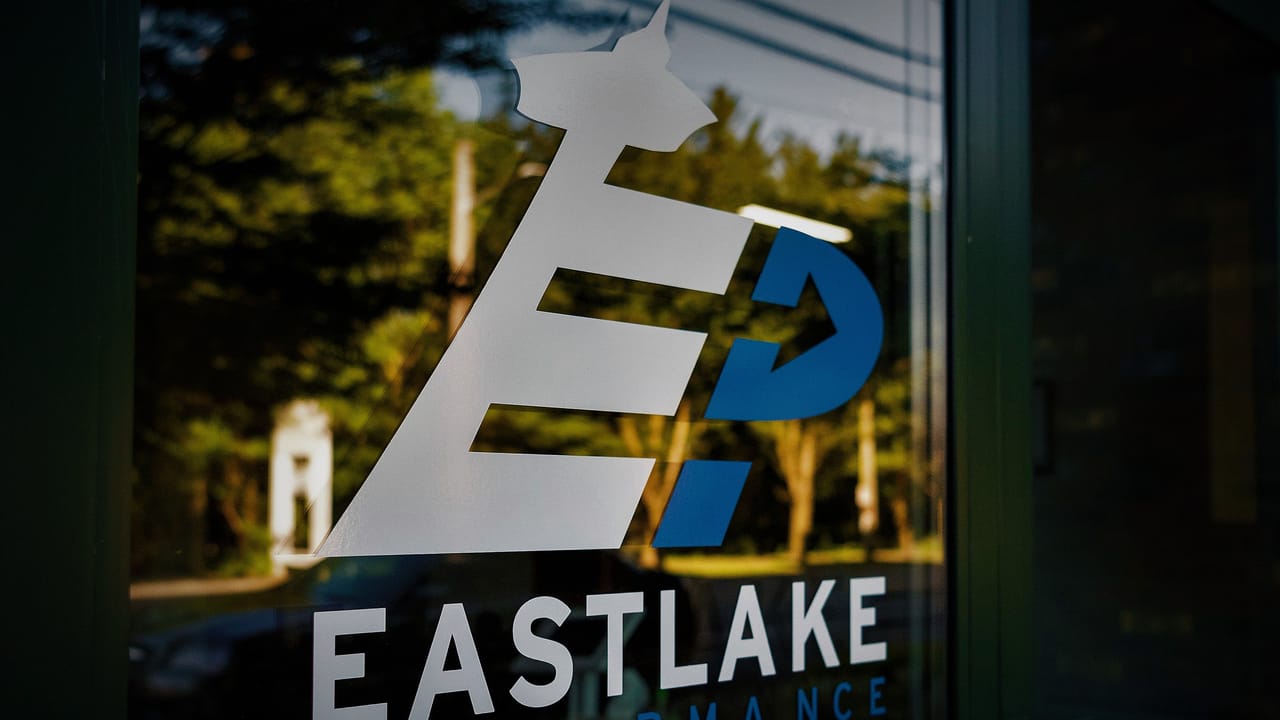 The glass entrance door to Eastlake Performance, with trees on Eastlake Avenue East reflected in it.